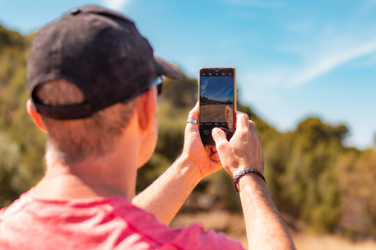 Man in cap photographing the natural landscape with his smartphone.