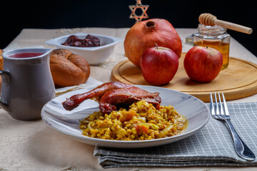 Spelled with a duck leg in a plate on the festive table for Rosh Hashanah next to grenades, gray apples, wine and challah.