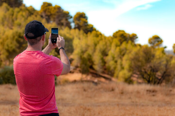 Man in cap and red T-shirt photographing the natural landscape with his smartphone.