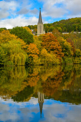 Church tower behind fall colored trees reflecting in river