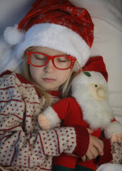 A lovely sweet girl in red glasses sleeping with a christmas toy and waiting for a miracle on a white background. Christmas holiday