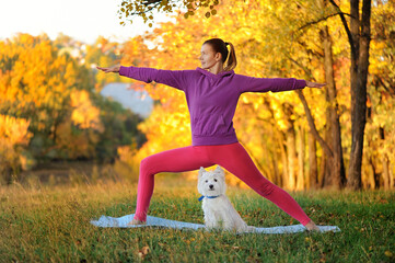 Full length picture of woman practicing hero yoga pose with her dog