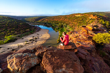 long-haired girl sits on top of a hill on the red rocks of kalbarri national park in western...