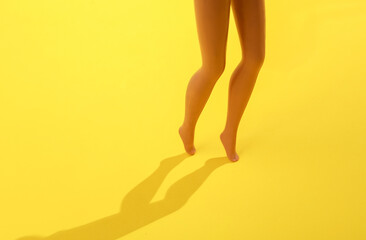 Doll legs on a yellow background with a shadow