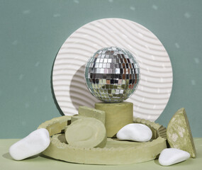 Disco ball on a podium with plaster geometric shapes on a two tone background. Creative party still life