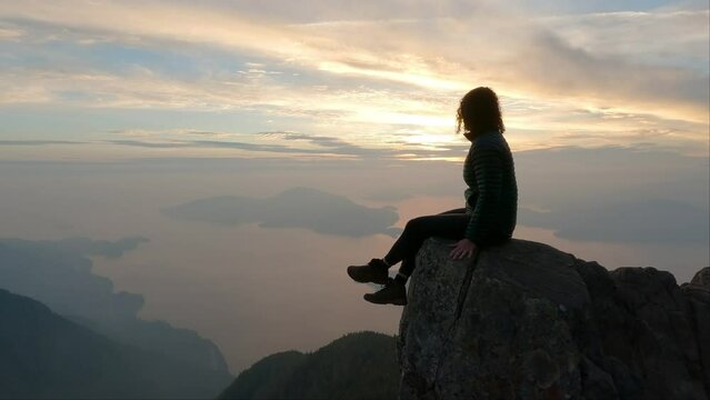 Adventurous Woman Hiker on top of Canadian Mountain Landscape on the West Coast of Pacific Ocean. Dramatic Sunset and smoky Sky. St. Mark's Summit near Vancouver, BC, Canada. Slow Motion Cinematic