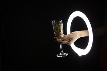Female hand holding glass with garland through led ring lamp on black background. Christmas Party concept