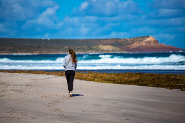 long-haired girl walks on the beach with massive cliffs in the background in kalbarri national park, western australia; walking on a paradise australian beach