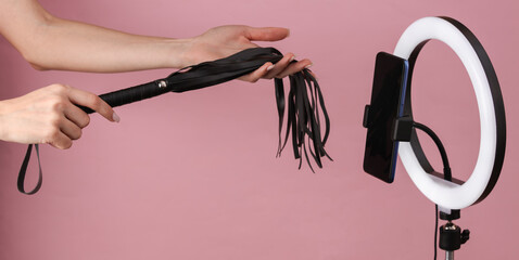 Sex blog. Female hands holding leather whip from sex shop, broadcasting to smartphone camera with...