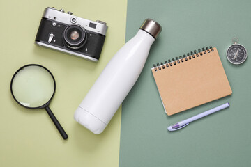 Hhiking equipment. Thermos bottle, camera, magnifier, notebook and compass on green background. Top view. Flat lay - obrazy, fototapety, plakaty