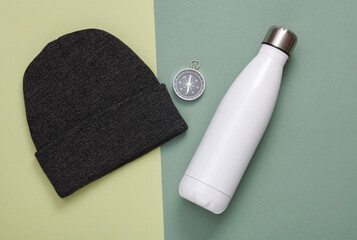 Camping equipment. Thermos bottle and compass with hat on green background. Top view