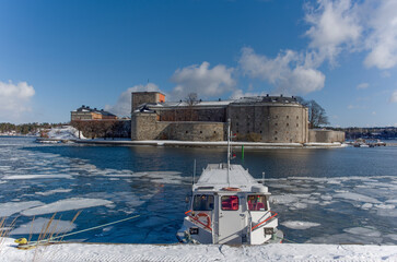 Winter view in Stockholm archipelago town Vaxholm, icy lake, snow, pier, 1700s fortress and...