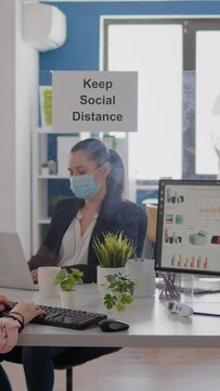 Vertical video Business team typing financial strategy on laptop, wearing face mask to prevent infection with covid19 while sitting at office desk. Coworkers keeping social distancing to avoid virus