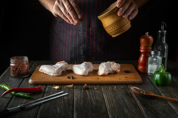 The cook adds salt to raw chicken wings. Cooking chicken nugget in the kitchen of a restaurant