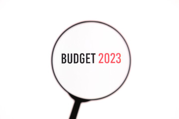 Phrase Budget 2023 through a magnifying glass on a white screen background. Economy, business concept