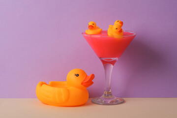 Cocktail glass with rubber ducks on two tone pastel background. Visual trend. Minimalistic aesthetic still life. Party concept. Fresh idea
