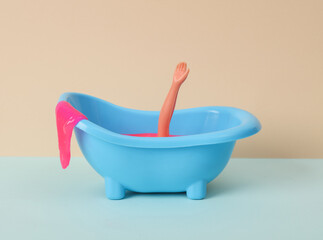 Creative layout, drowning doll in the bath on two tone pastel background. Visual trend.