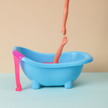 Creative layout, drowning doll in the bath and and a helping hand on two tone pastel background. Visual trend.