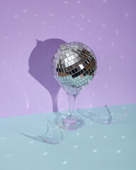 Creative party layout with broken cocktail glass and disco ball on two tone pastel background. Visual summer trend. Minimalistic aesthetic still life. Reflection, shadows