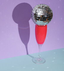 Creative summer layout, glass with disco ball on two tone pastel background. Visual trend. Minimalistic aesthetic still life. Party concept. Fresh idea