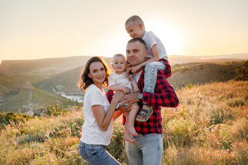 Happy family spending time together in the nature, mother father daughter and son have fun, playing with kids in vacation against the background the grass, mountain and sunset