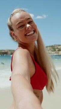 Young European woman in bikini on the beach in summer. Happy young woman smiling at the sea. Tanned blonde girl in swimwear enjoying the beach. Vertical video.