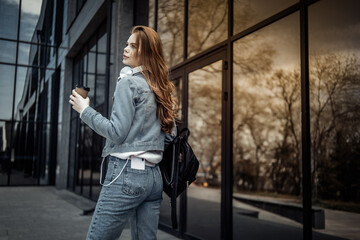 Fototapeta na wymiar Young beautiful woman in denim jacket and holding coffee cup near the windows of the business center