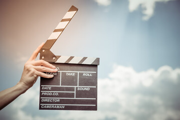 Hand holds movie board on background of blue sky with clouds.