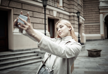 Young stylish blonde woman makes selfie on smartphone in the city