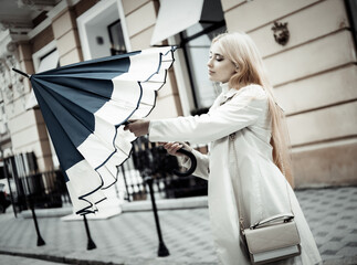 Young blonde woman in anticipation of rain opens umbrella in city
