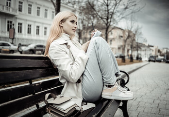 Fototapeta na wymiar Stylish young woman tsudent sits on a bench and writes in notebook