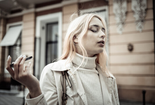 Young woman smokes smoke an electronic cigarette in the city