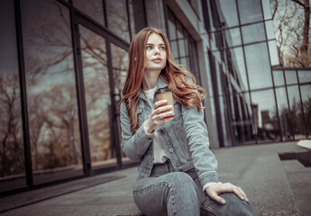 Young pretty woman sits on the stairs near the business center and drinks coffee