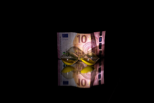An hourglass and ten euros lie on a mirror in the dark, time is money, business