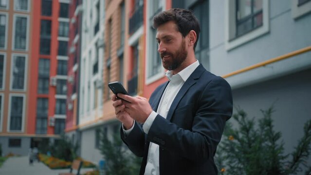 Handsome successful businessman caucasian man stand near modern residential building in city working outdoor use phone digital mobile app on way search information online texting messages distant chat