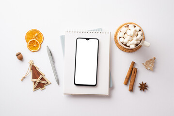 Top view photo of smartphone notepad pen cup of cocoa with marshmallow dried orange slices acorn...