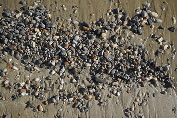Sunny autumn day on the Aegean Sea. Texture of wet pebbles on beach sand. Surf