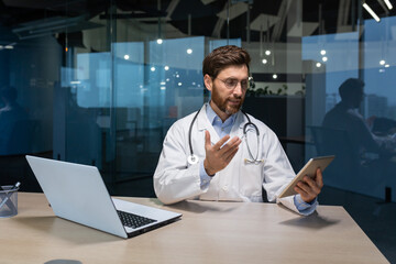 Video call online consultation of a doctor, an experienced doctor works inside the office of a modern clinic, gives a consultation remotely, uses a tablet to communicate