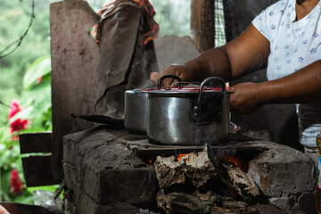 close-up of the hands of a latin woman, a brown-skinned peasant, holding an iron pot on top of a traditional stove, commonly used for cooking on a colombian farm, using wood as fuel.