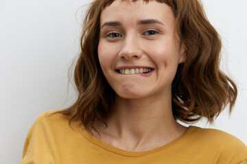 horizontal close-up portrait of a beautiful, playful, tanned woman in a yellow T-shirt on a light background sexually biting her lower lip
