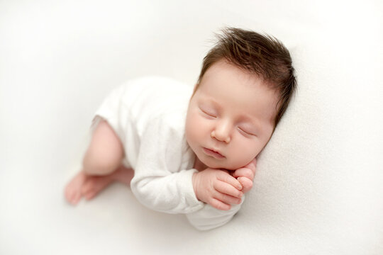 Top view of a newborn baby girl lying in a white bodysuit on a white bed. Beautiful portrait of a little sleeping girl with closed eyes 7 days, one week. Photography in macro studio.