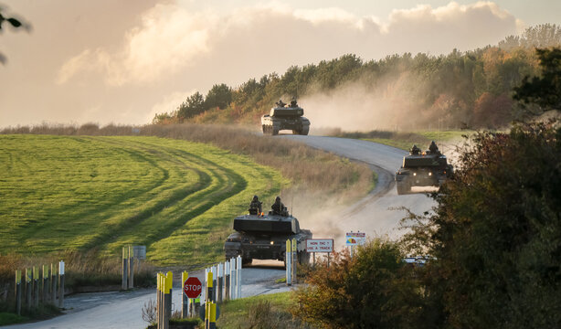 a section of British army Challenger 2 ii FV4034 tanks descend a country track to a road crossing, late afternoon autumn sky, Wiltshire UK