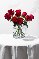 Fototapeta premium Red roses in a vase on a round table on a white background