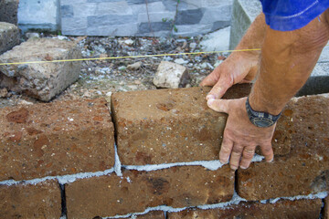 Image of the hands of a bricklayer who builds a wall with tuff bricks following the thread for...