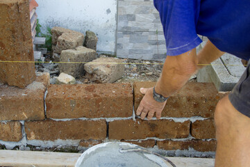 Images of the hands of an old mason while with cement he builds a low wall with tuff bricks. Man at work
