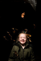 Young girl throwing dying leaves in the air at autumn time in a studio setting.