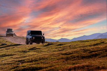 off-road black car driving on a dirt track in the mountains with a spectacular sky at sunset. car adventure trip