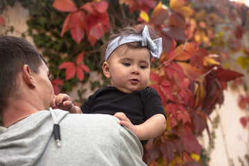 Happy father play with the baby. The man holding the toddler in the hands and have fun against the background red leaves