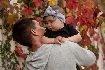 Happy father play with the baby. The man holding the toddler in the hands and have fun against the background red leaves