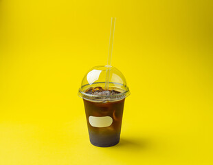 cold tea in a plastic glass with a straw on a yellow background